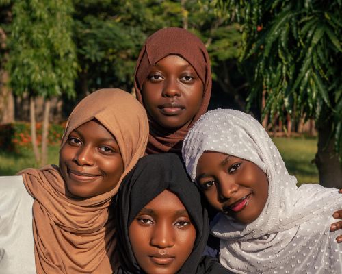 Free Group of four women wearing hijabs smiling brightly outdoors with natural greenery background. Stock Photo