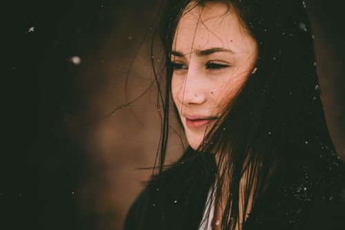 Free Portrait of a young woman with dark hair, pensively looking amidst falling snow, evoking winter solitude. Stock Photo