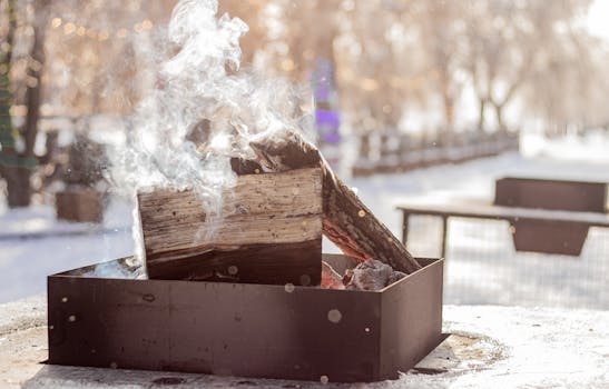 A cozy winter bonfire with smoking wood outdoors, surrounded by snowy scenery.