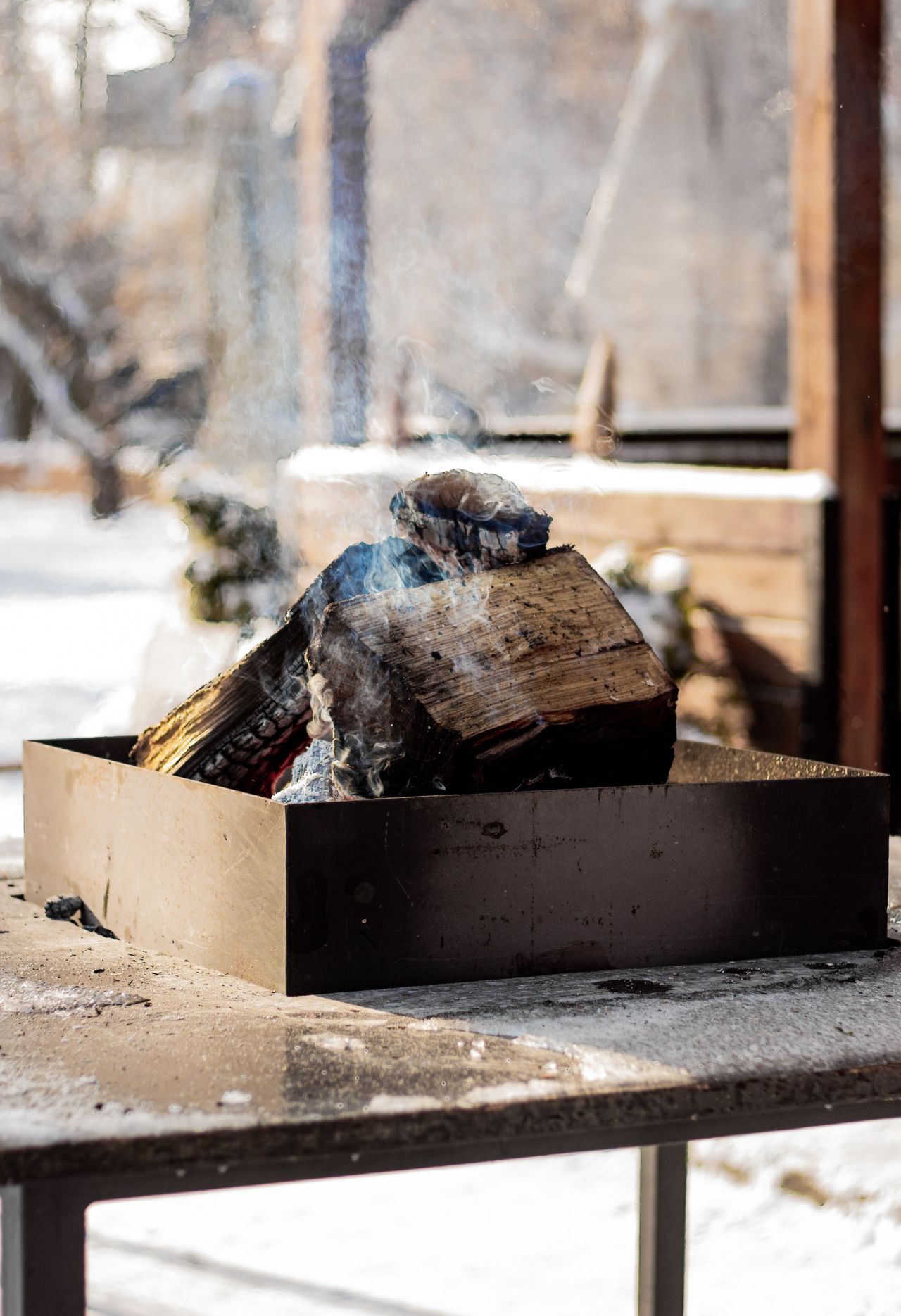 Metal fire pit with smouldering logs in a snowy backyard