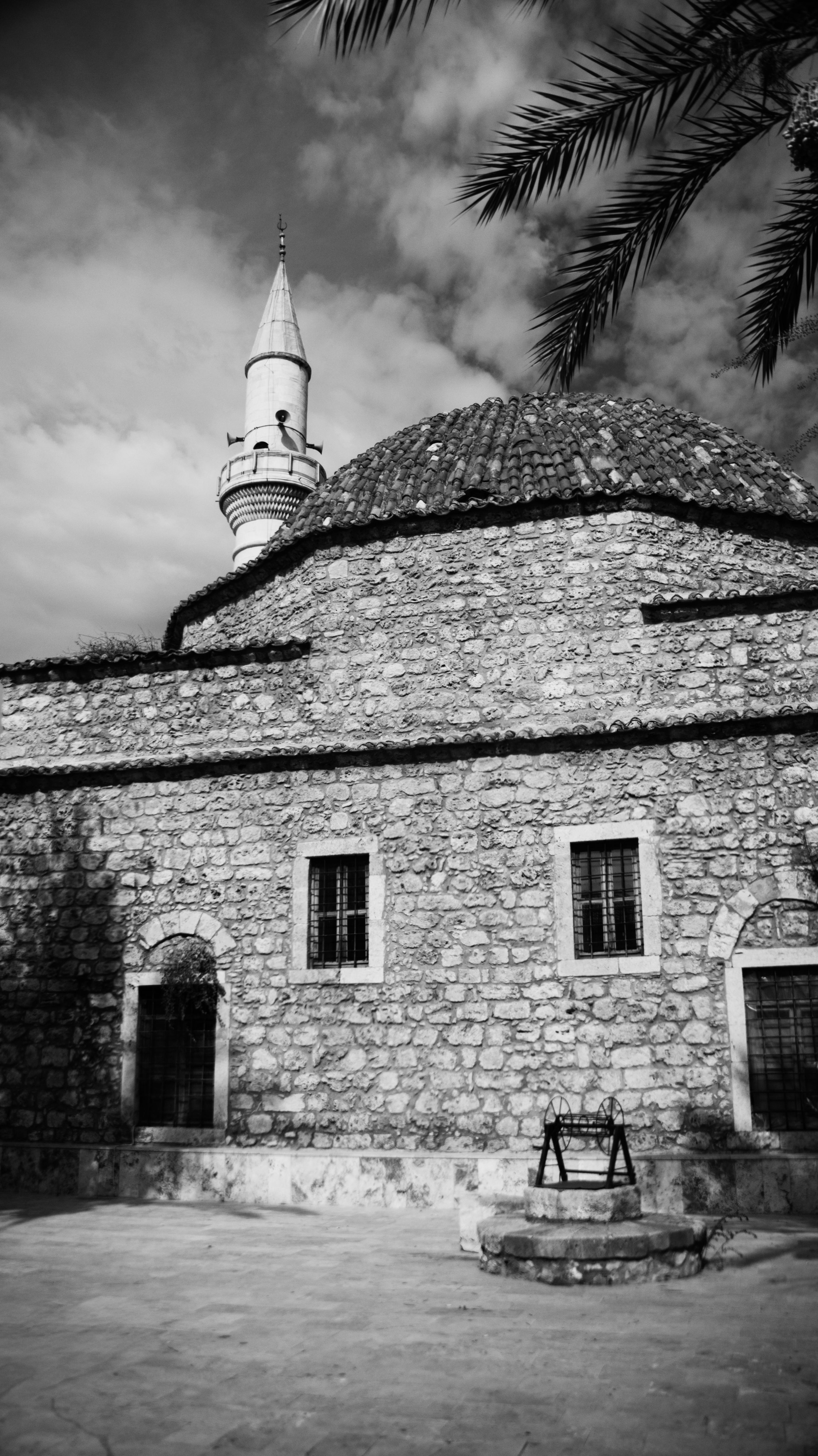 Black and white image of a historic stone mosque with a distinctive minaret in an outdoor setting.
