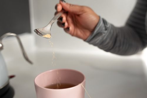Free Unrecognizable female in casual clothes holding tea spoon and pouring sugar into ceramic cup with hot tea  on light kitchen Stock Photo