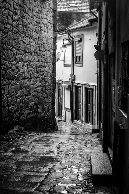Moody black and white photograph of a narrow cobblestone alleyway in a historic European town.