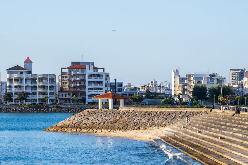 Charming coastal cityscape with waterfront steps, modern buildings, and blue sea under a clear sky.