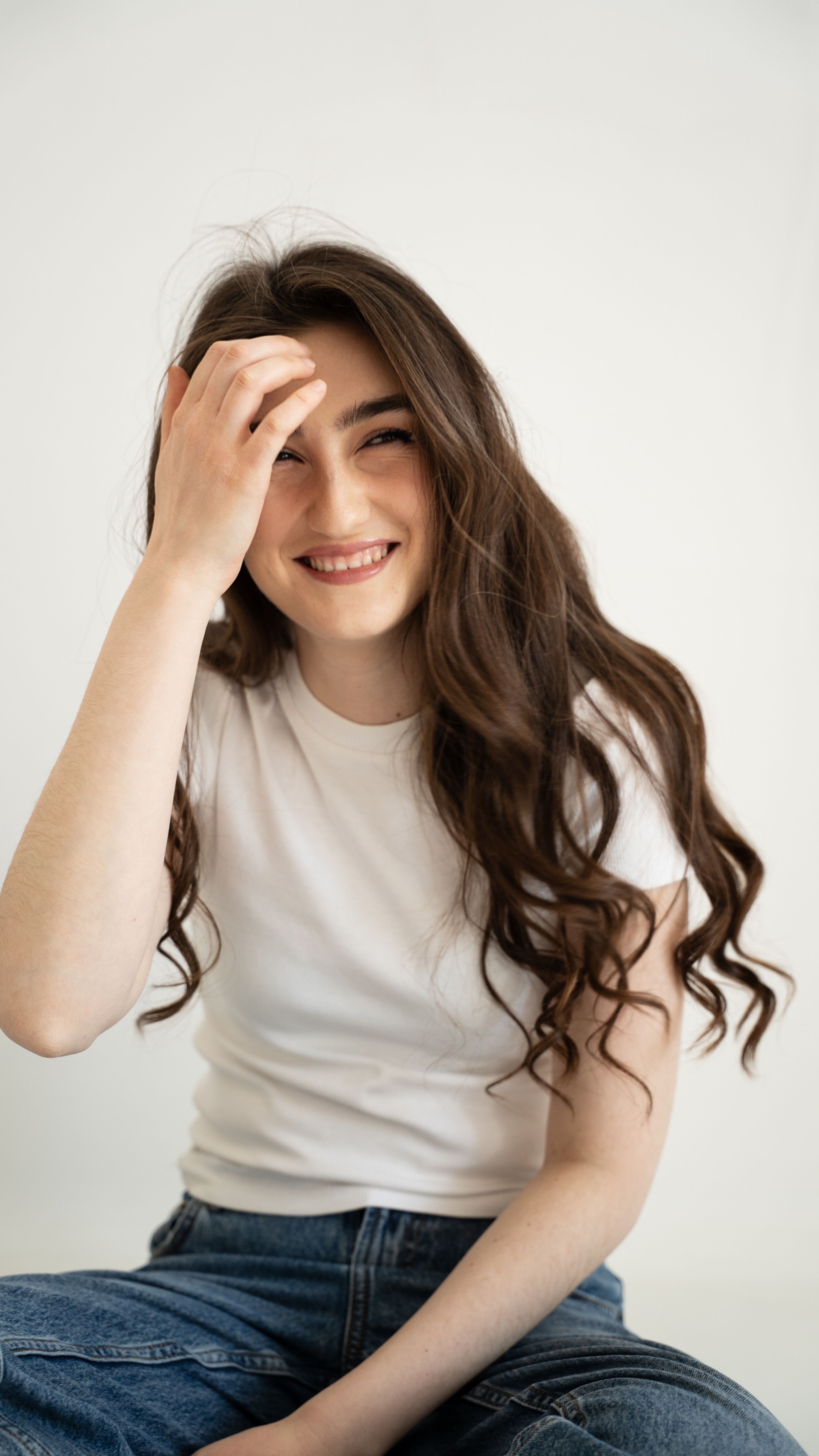 Happy young woman with long hair smiling, wearing a white shirt and jeans.