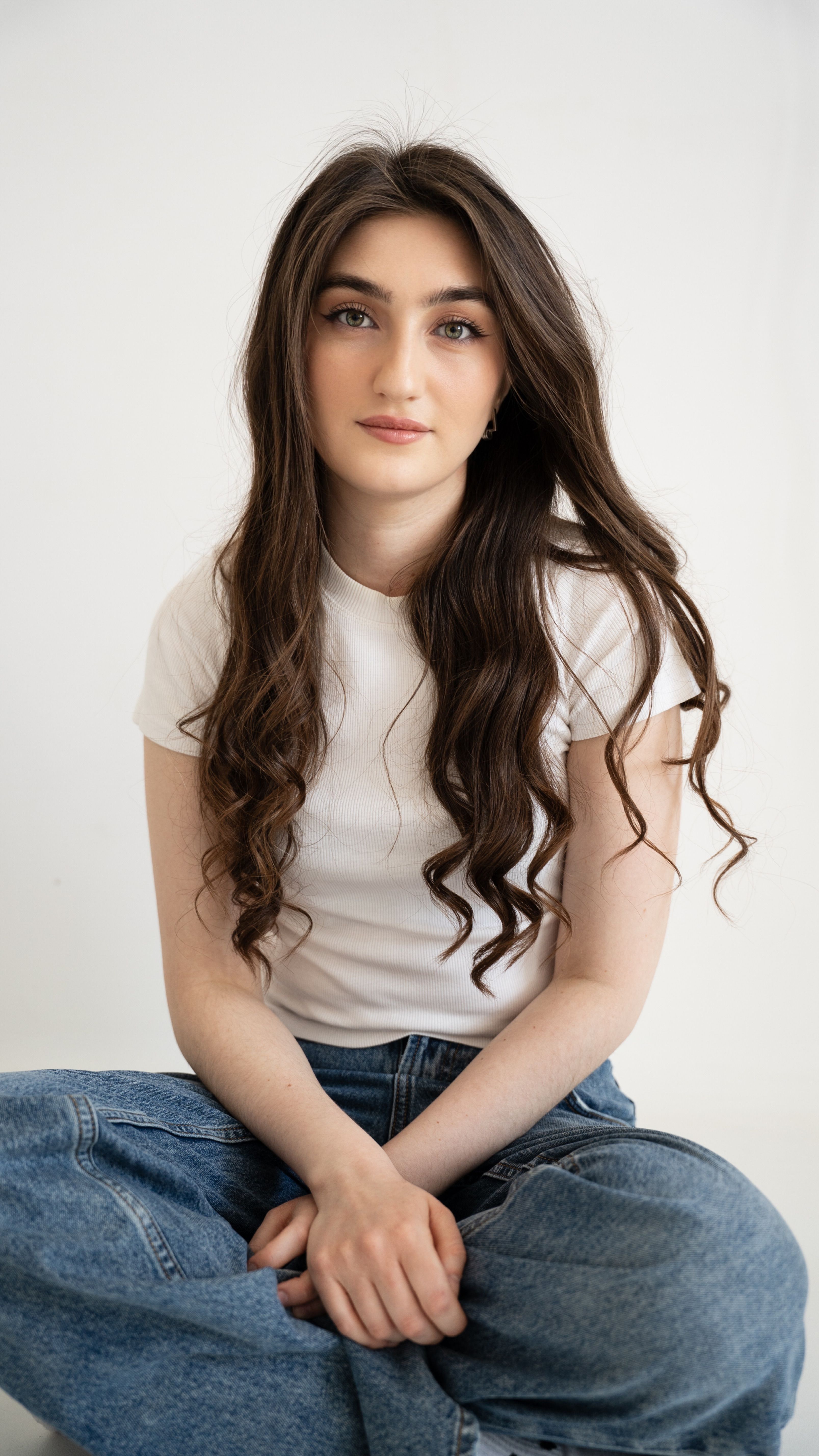 Charming portrait of a young woman sitting cross-legged in casual attire, exuding a calm vibe.