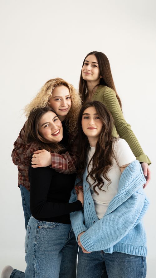 Free Four smiling teenage girls embracing joyfully inside a bright room. Stock Photo