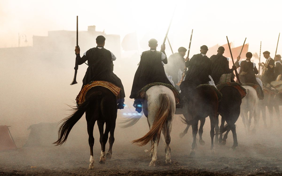 Free A group of horsemen perform the traditional Moroccan fantasia during sunset, creating dramatic dust clouds. Stock Photo