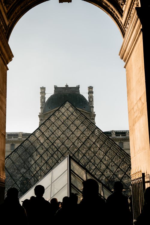 Free Visitors silhouetted at the iconic Louvre Pyramid entrance in Paris during the day. Stock Photo