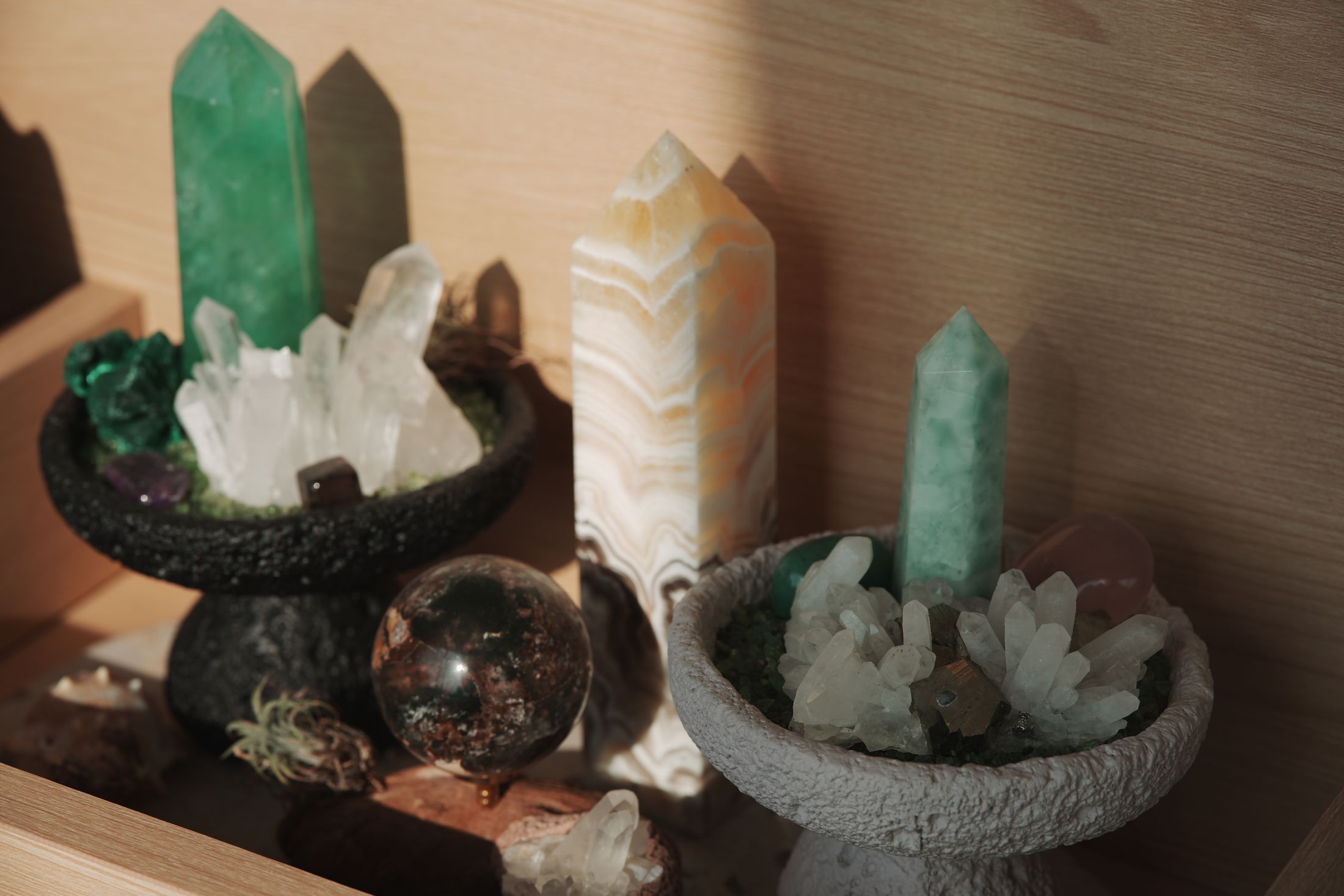 木質層架上陳列綠色水晶柱、白水晶簇、條紋水晶柱與水晶球，柔和室內光