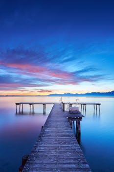 Serene view of a tranquil wooden pier extending into a calm lake during sunrise in Bavaria, Germany.