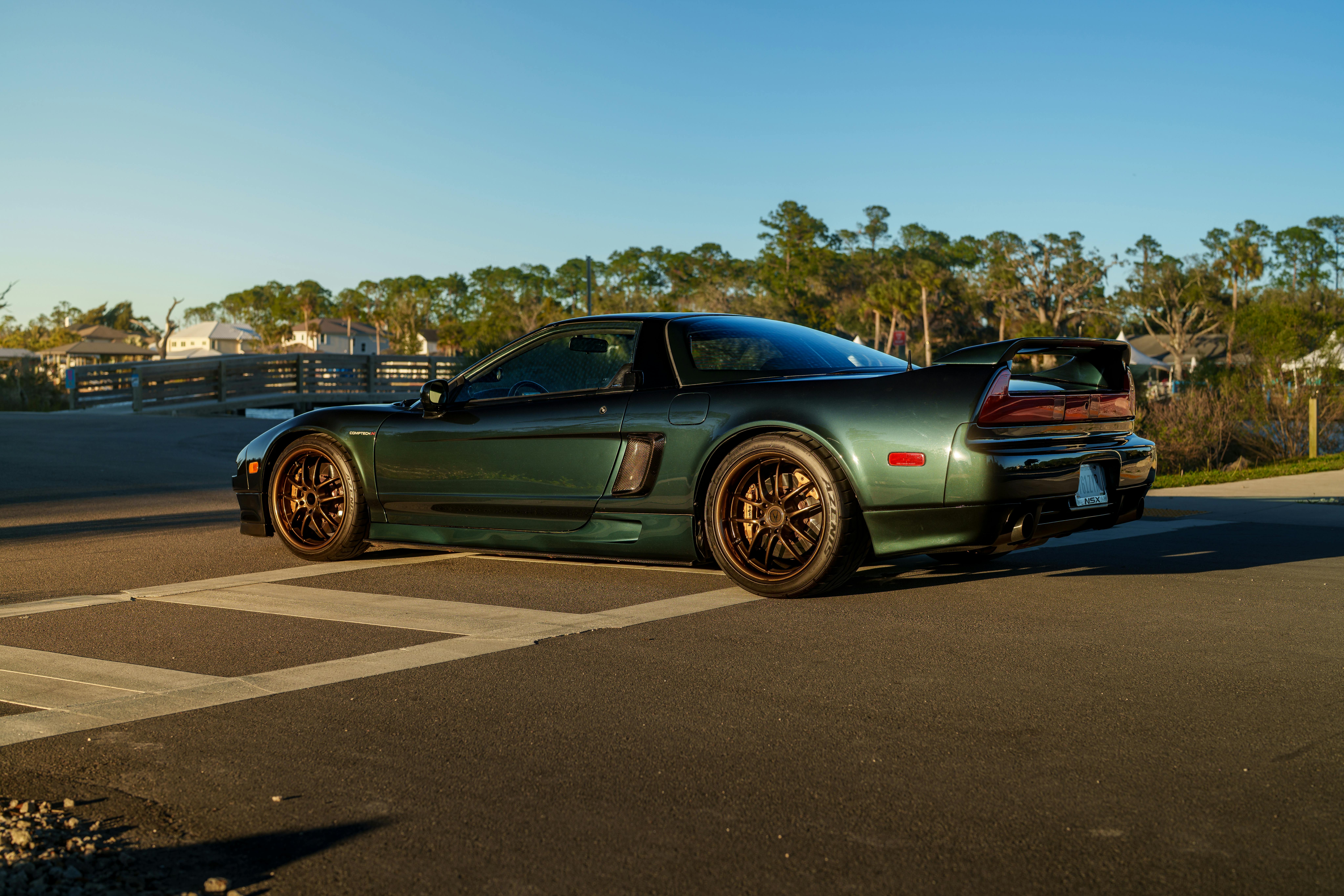 A sleek green sports car parked outdoors in the sunlight with trees in the background.