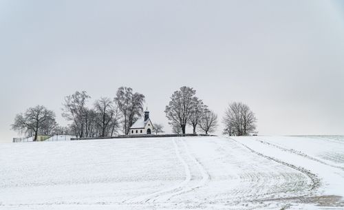 Free A picturesque chapel on a snowy hill surrounded by bare winter trees under an overcast sky. Stock Photo