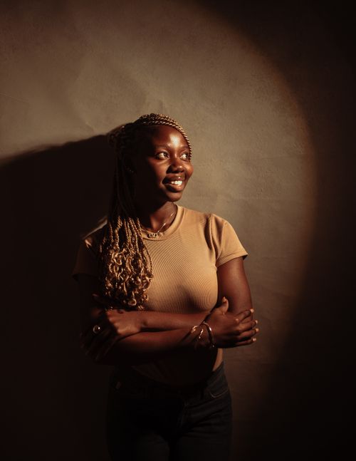 Free A woman with braided hair smiles warmly in a dramatic, soft-lit portrait indoors. Stock Photo