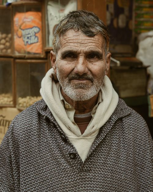 Free Elderly man in a cozy sweater stands in a bustling market setting. Stock Photo