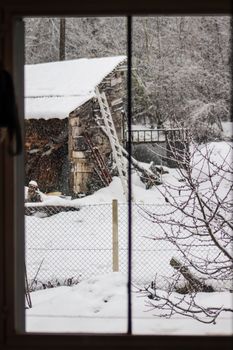 A charming view of a rustic cabin in winter, seen through a window with snow-covered landscape.