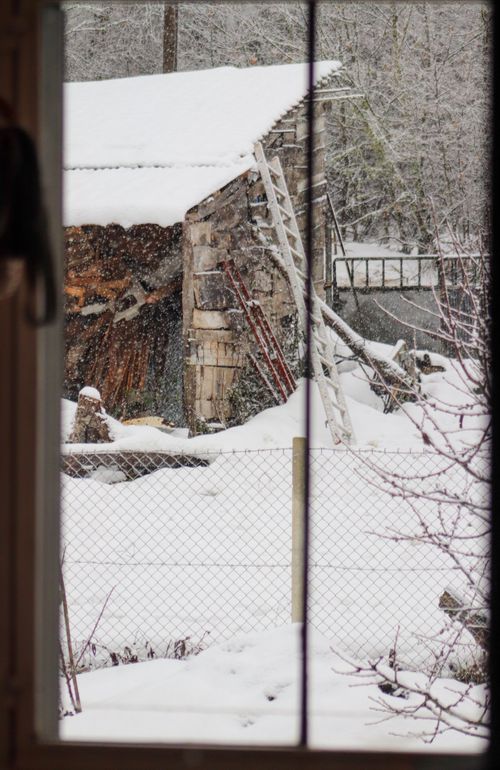 Free View of a rustic cabin in snow through a window during a winter day, showcasing a serene and peaceful landscape. Stock Photo
