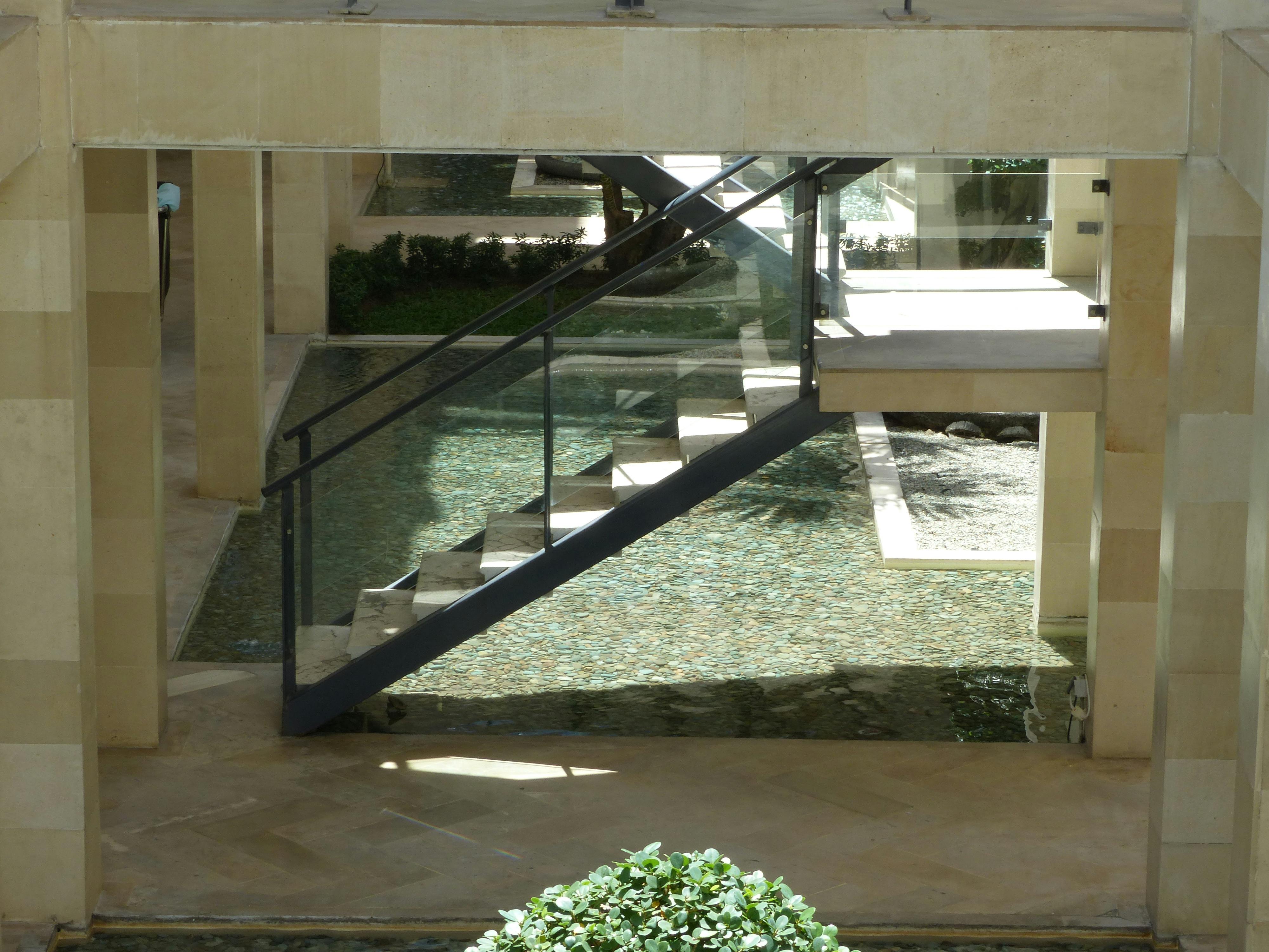 Bezpłatne Nowoczesne schody ze szklaną balustradą nad odbijającym światło elementem wodnym wewnątrz budynku. Zdjęcie z galerii