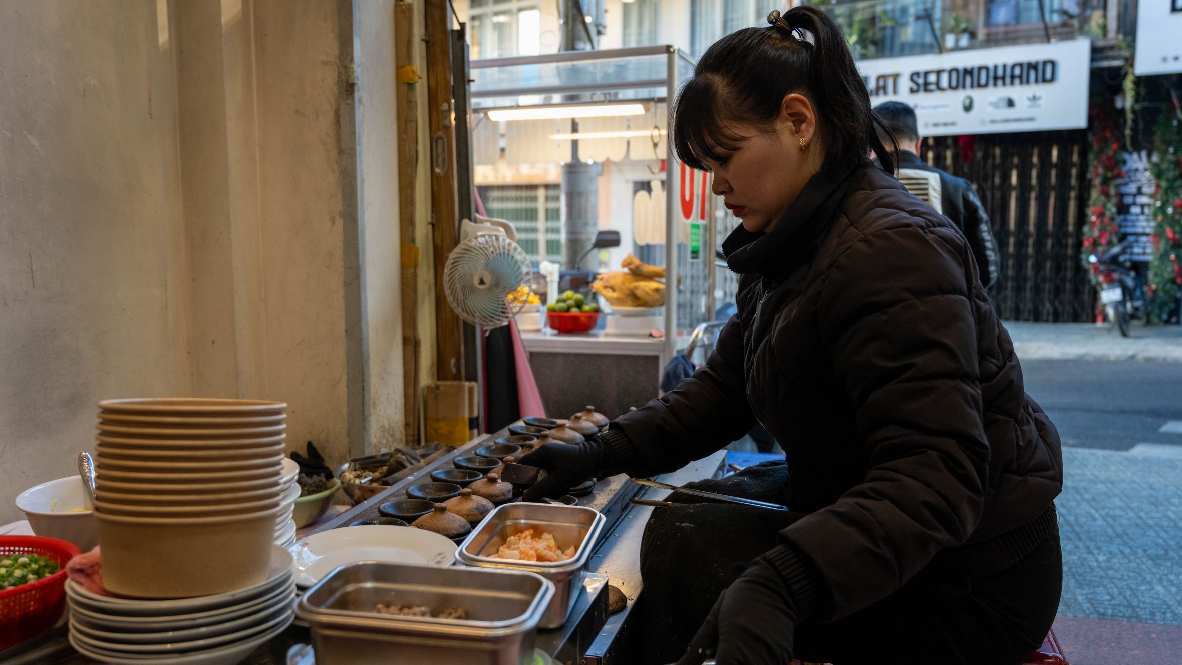 Female vendor prepares traditional street food outdoors in Dalat, Vietnam.