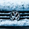 A close-up of a silver Volkswagen logo on a car grille heavily covered in snow and ice.