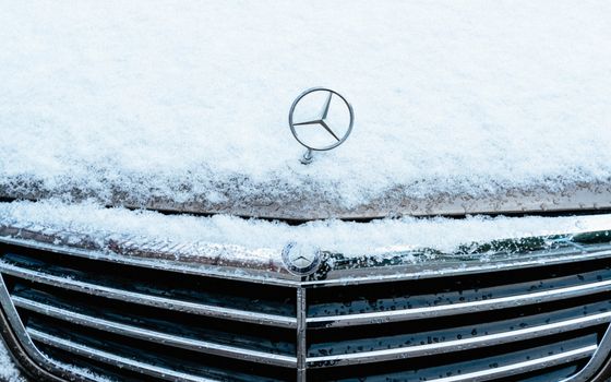 Snow-covered car hood with emblem in winter, captured in Spain.