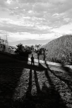 Black and white photo of human shadows cast on a hillside with a mountain vista.