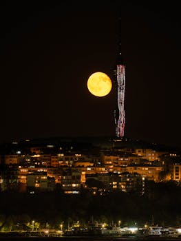 Full moon illuminating a cityscape with a prominent skyscraper at night.