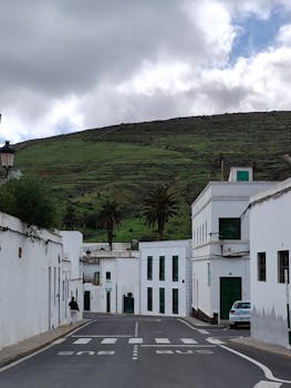 Charming street view with white architecture, palm trees, and hilly backdrop.