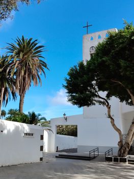 A picturesque Mediterranean church tower with palm trees under a vibrant blue sky.