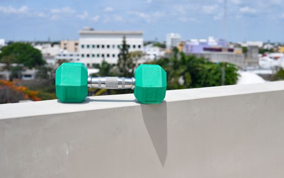 Green dumbbell on a wall overlooking a cityscape in Cancún, Mexico, under a bright blue sky.