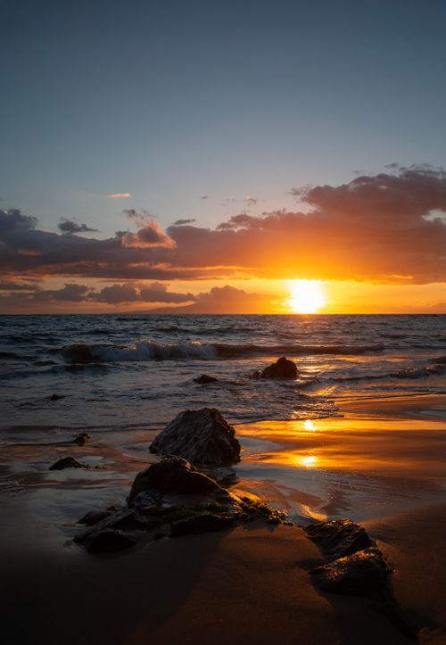 Free Stunning sunset over a rocky beach in Hawaii, reflecting warm colors on the ocean. Stock Photo