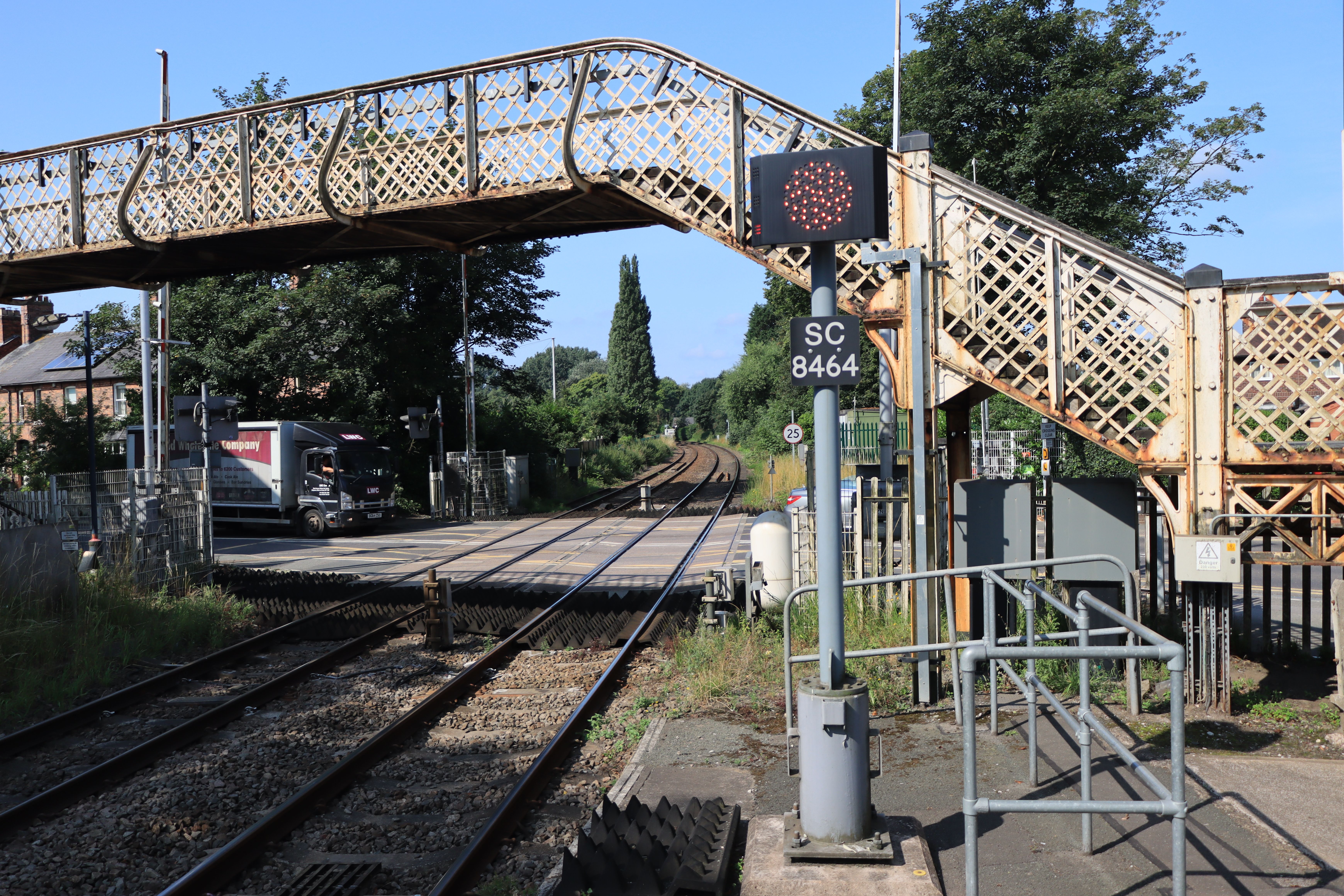A picturesque railway crossing in Nantwich, England, featuring a classic iron overpass and lush greenery.