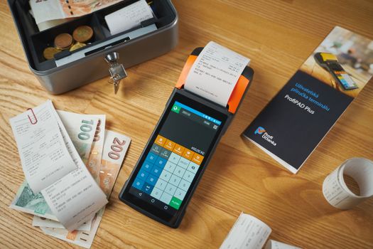 A modern payment terminal with receipts, cash, and manual on a wooden table.
