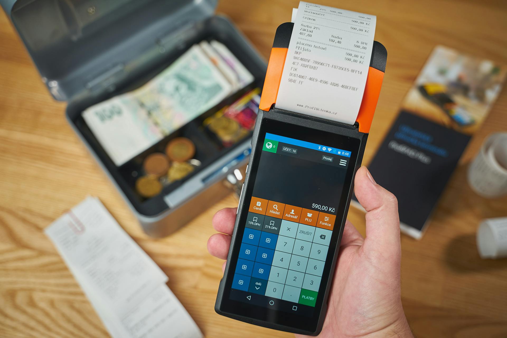 Close-up of a handheld payment terminal printing a receipt, with cash and coins visible.
