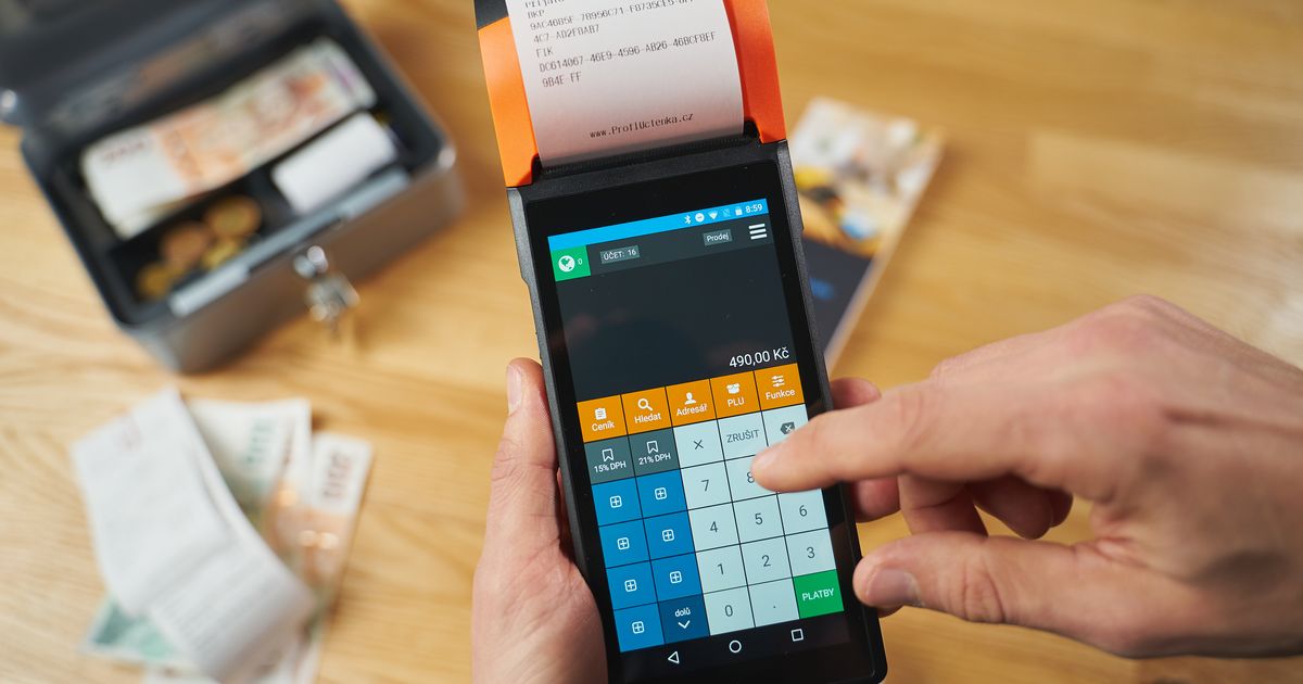 A close-up of a hand using a payment terminal with currency notes and a money box in view