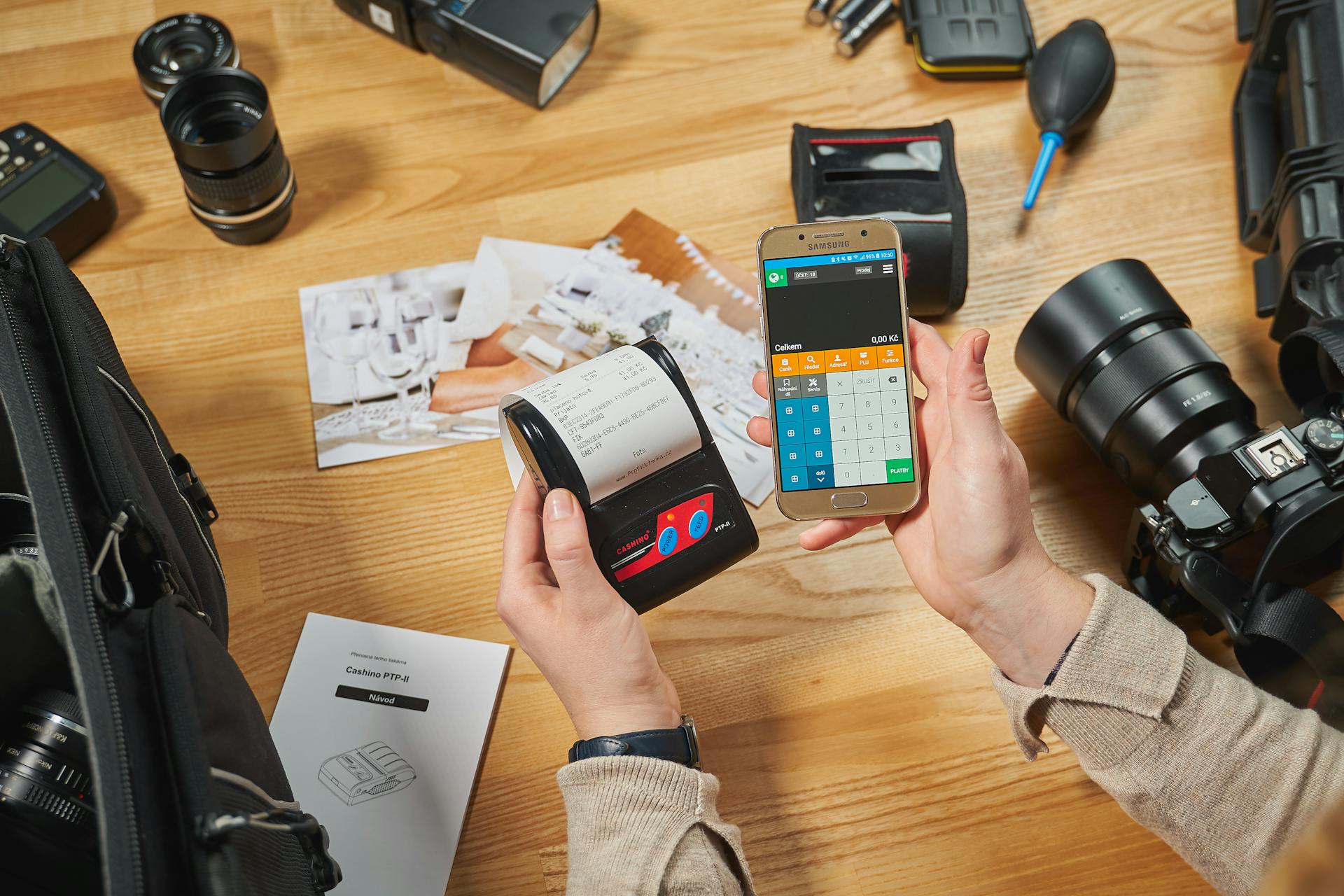 Person using smartphone and printer for mobile payment amidst photography equipment on desk.