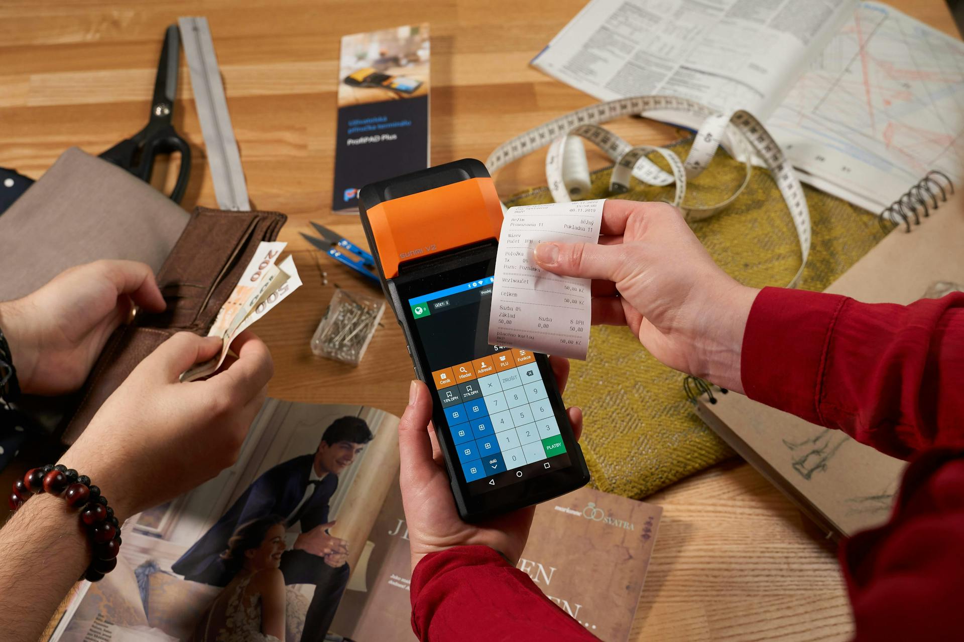 Tailoring shop scene with hands holding a payment terminal and cash, symbolizing a transaction.