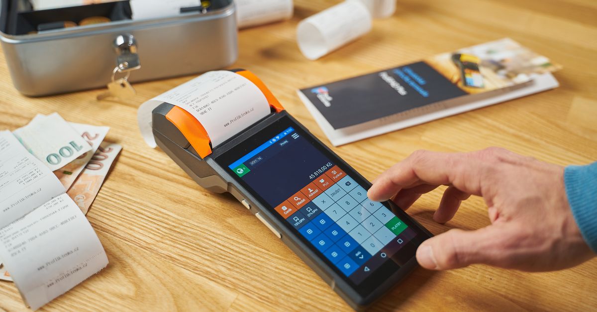 Person using a digital payment terminal on a wooden desk with cash and receipts visible. — illustrating receipt creator
