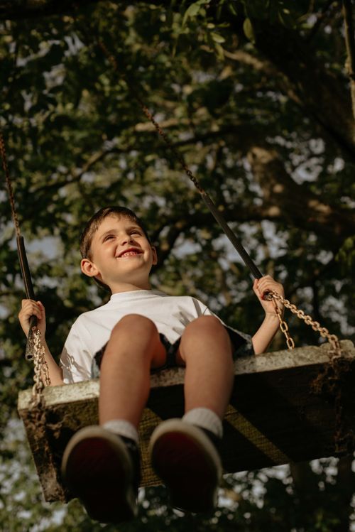 Free A young boy enjoying a swing outdoors with a joyful smile under lush trees. Stock Photo