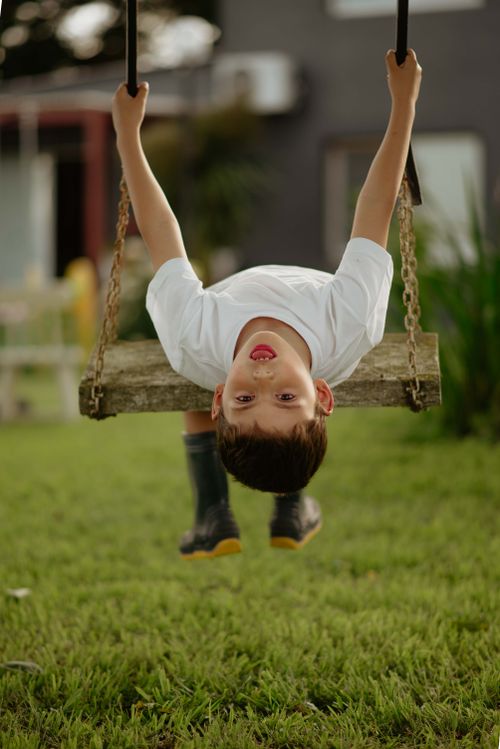 Free Playful child hanging upside down on a swing in a garden, enjoying a sunny day outdoors. Stock Photo