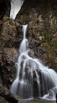 A serene waterfall cascades down rocky cliffs surrounded by lush greenery.