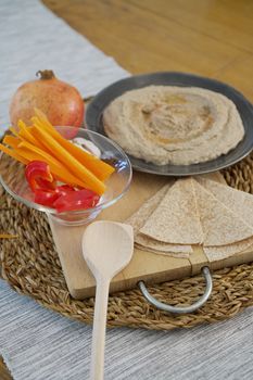 A delicious spread of hummus, sliced vegetables, and flatbread on a rustic table.