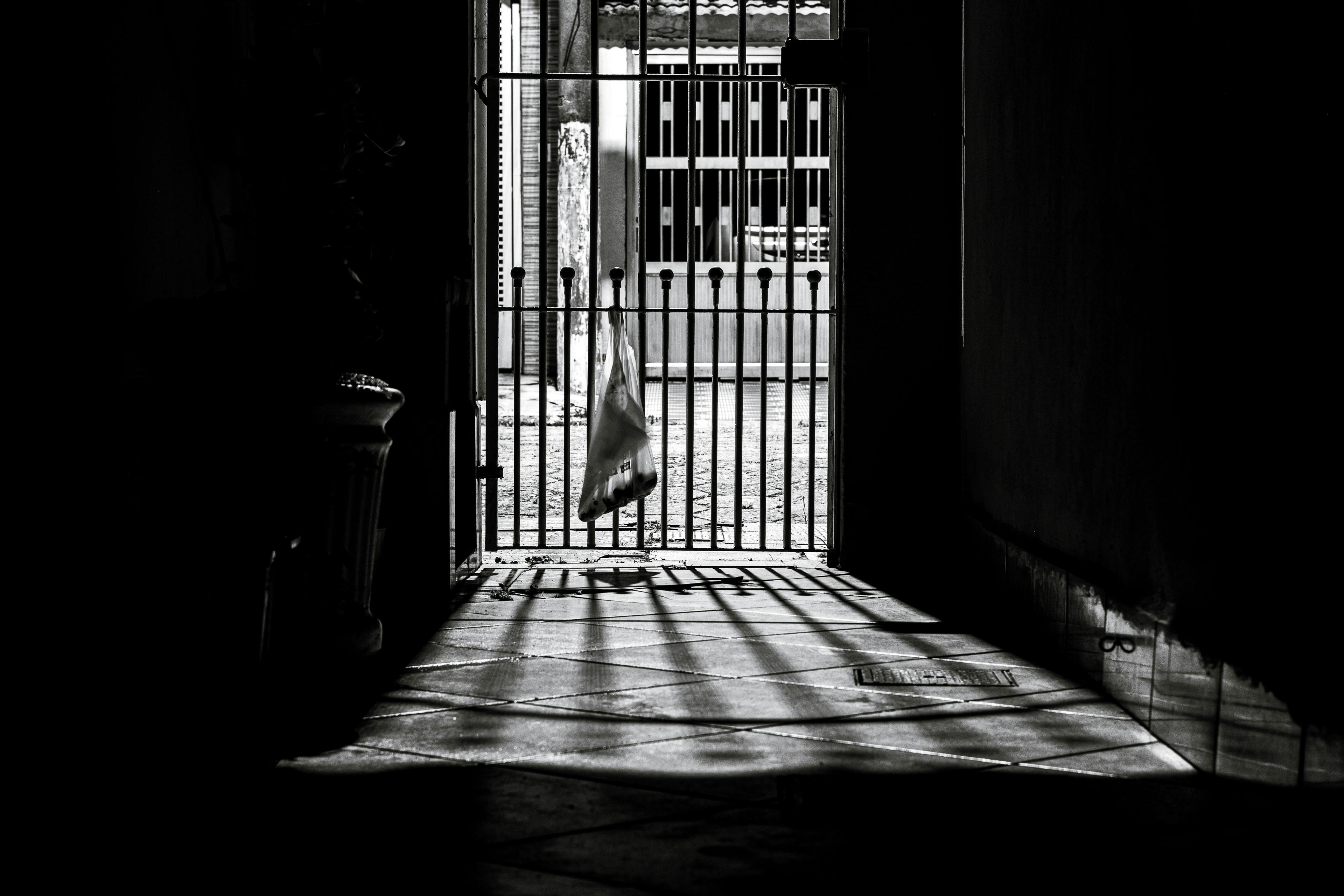 Dramatic black and white photo of a gated entrance with contrasting light and shadow.