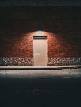 A glowing metal door on a brick wall at night, creating a mysterious urban scene.