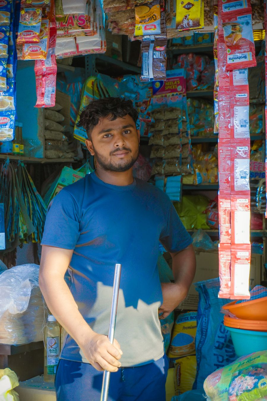 Indian shopkeeper standing among hanging goods in a store