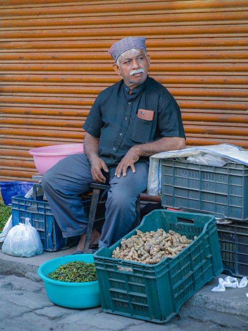 Free Older male street vendor selling spices and produce in outdoor market setting. Stock Photo
