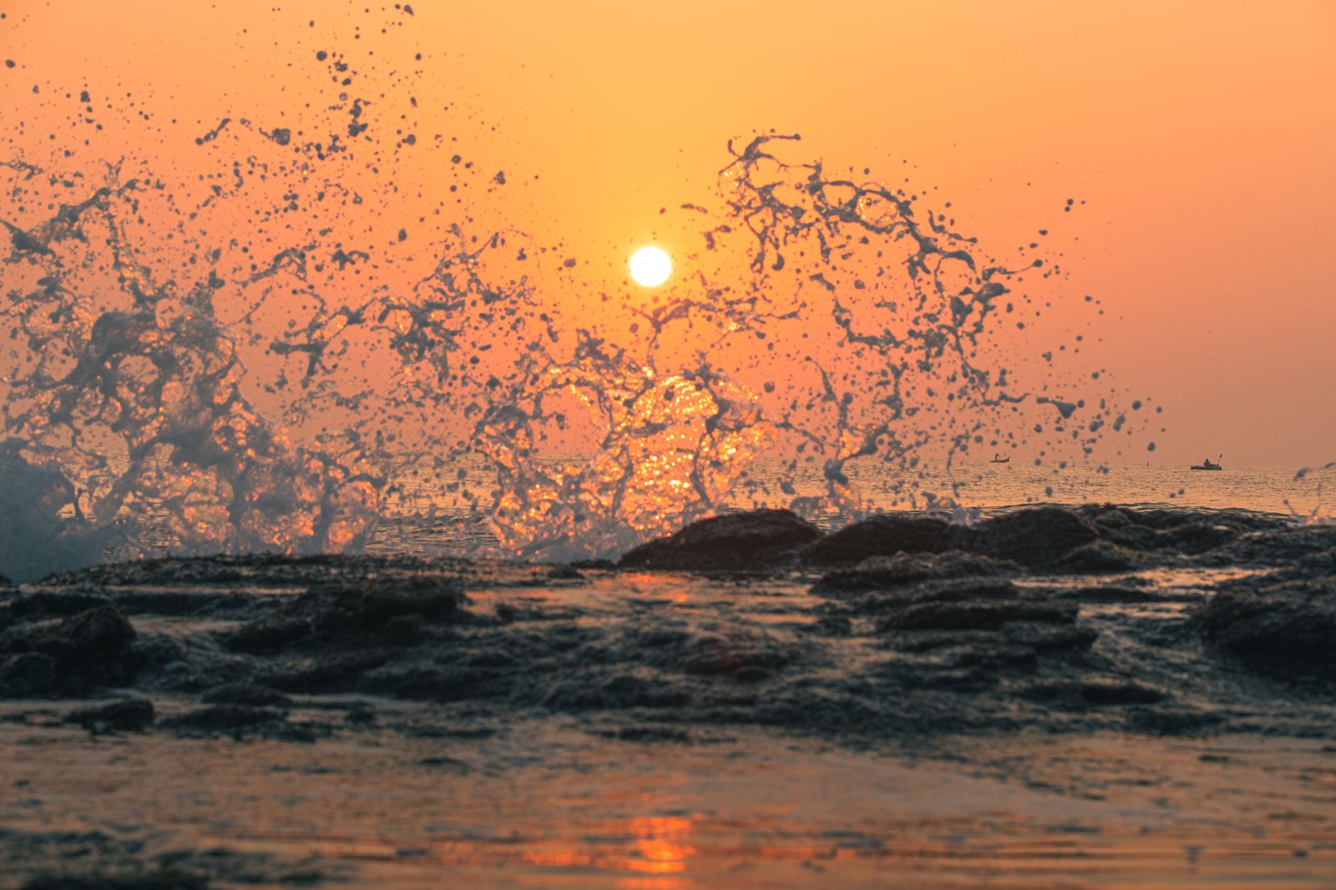 Captivating ocean waves splashing against rocks at sunrise, creating a dramatic scene.