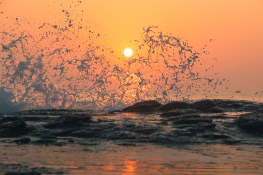 Captivating ocean waves splashing against rocks at sunrise, creating a dramatic scene.