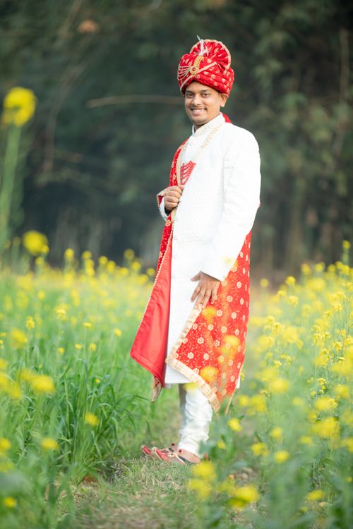 Free Indian groom in traditional attire standing in a vibrant mustard field. Stock Photo