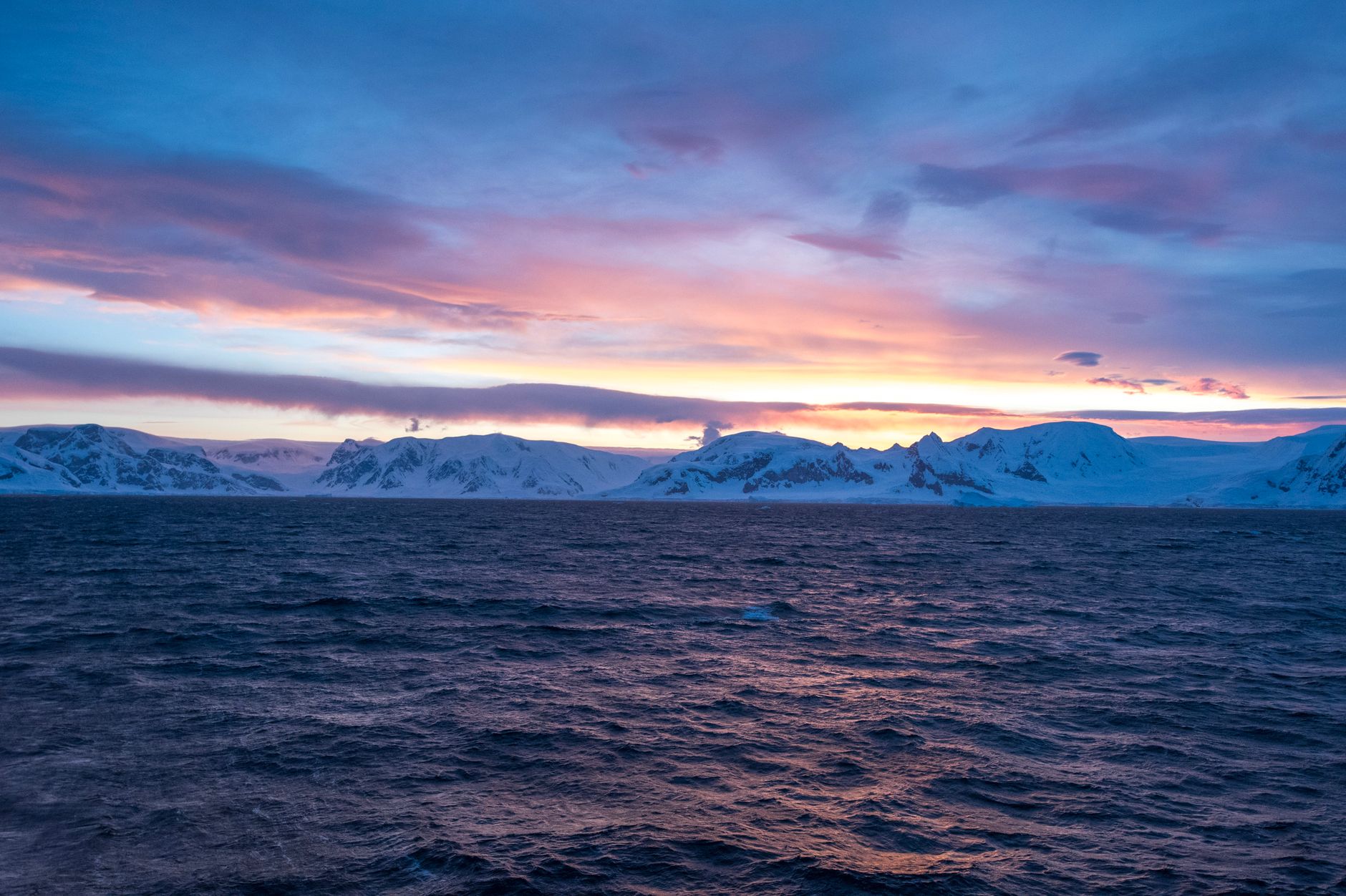 Vibrant sunrise over Antarctic mountains and ocean, showcasing nature's beauty and tranquility.